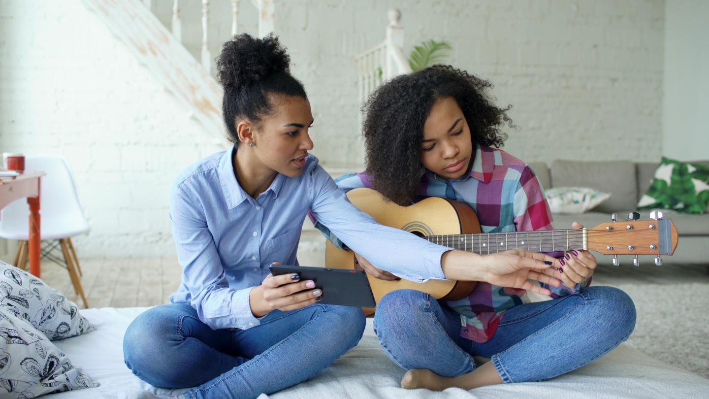 Two adults play an instrument while sitting on the floor