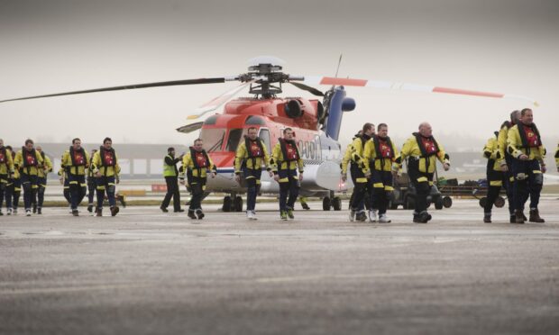 Offshore workers with a CHC Scotia helicopter at Aberdeen heliport.