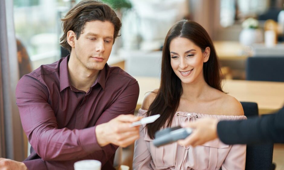 Woman sitting grinning as man pays for their lunch with his credit card