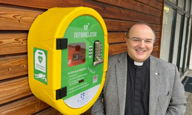 Father Domenico Zanre with the defibrillator mounted on the wall outside the church.