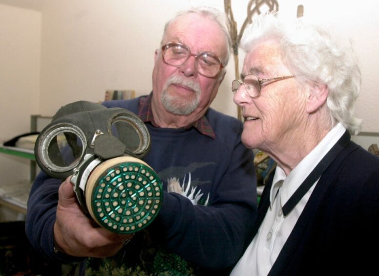 Ted Munyard, who also loved history, shown holding a gas mask while an elderly lady looks on.