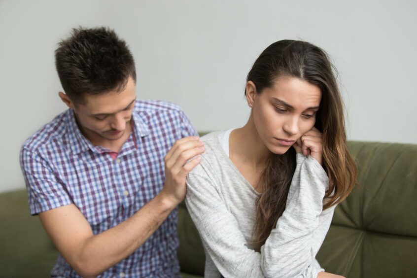 Man putting supportive hand on woman's shoulder after she's depressed from miscarriage