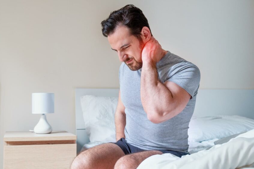 Man holding onto his stiff, painful neck when getting out of bed