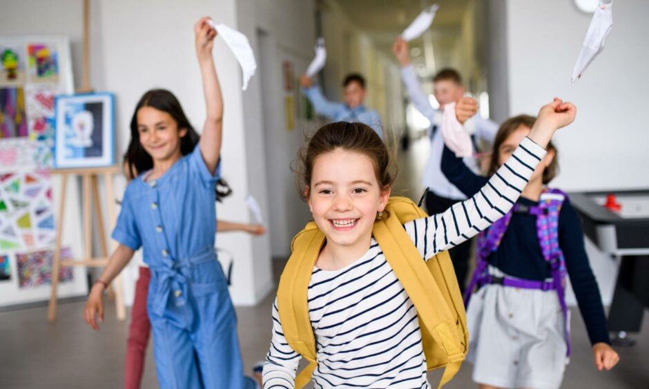 Children run out of clas with face masks held over their heads happily. Shutterstock ID 1746069452