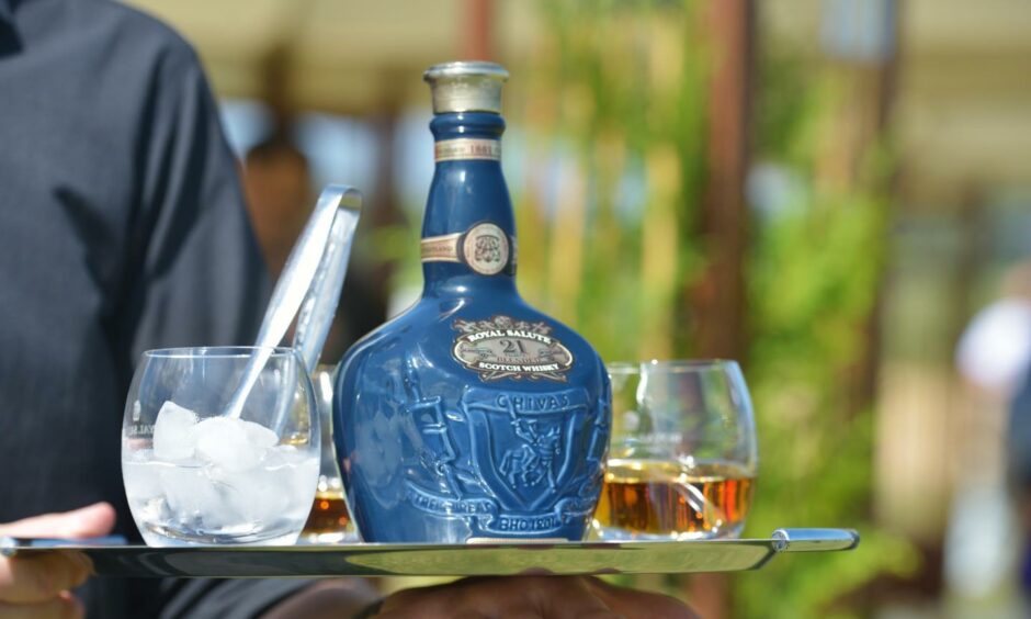 A waiter carrying a blue bottle of Royal Salute on a tray with three glasses