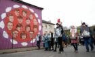 People take part in a march to commemorate the 50th anniversary of Bloody Sunday, holding photographs of some of the victims as they pass a mural dedicated to those who died (Photo: Peter Morrison/AP/Shutterstock)