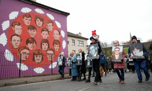 People take part in a march to commemorate the 50th anniversary of Bloody Sunday, holding photographs of some of the victims as they pass a mural dedicated to those who died (Photo: Peter Morrison/AP/Shutterstock)