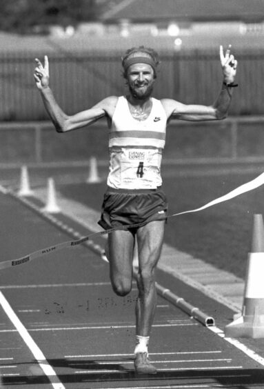 Fraser Clyne crossing the finishing line and holding up peace sign in black and white.