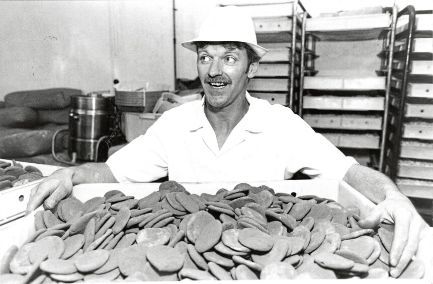 Black and white photo of a man smiling at the camera while holding a tray of lucky tatties