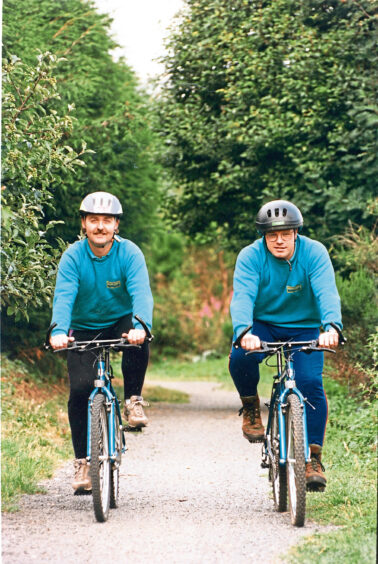 Coloured photo of two men riding bikes towards the camera