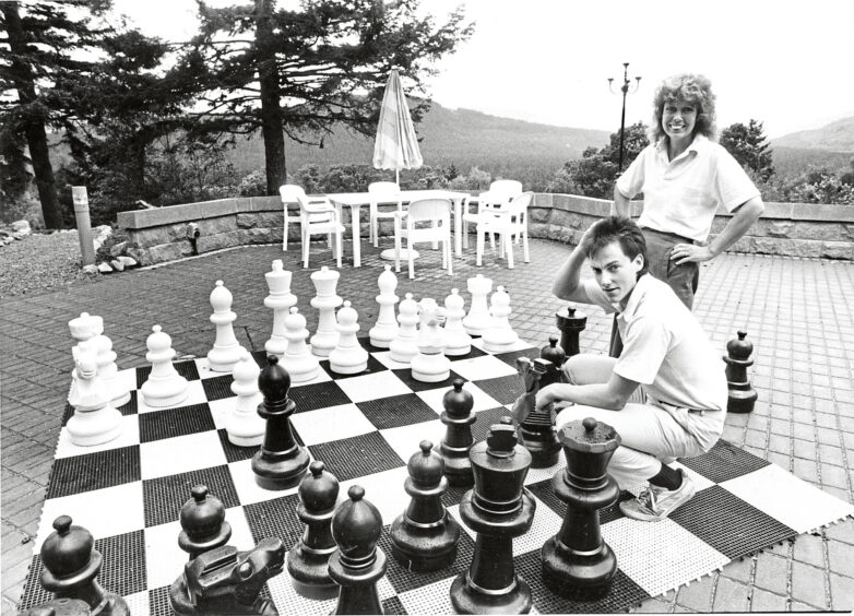Black and white photo of a man and a woman playing chess on a large garden chessboard mat