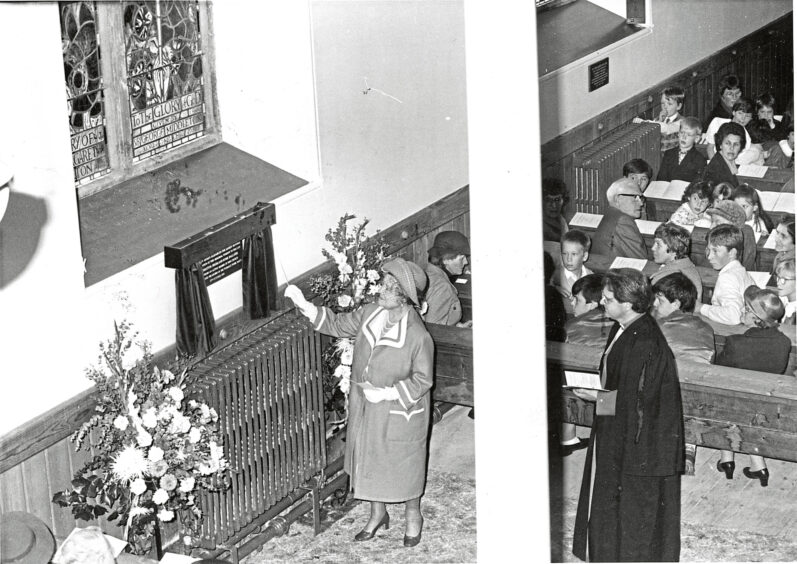 Black and white photo of the Queen Mother in Glenmuick Church with parishioners and a minister watching as she unveils a plaque