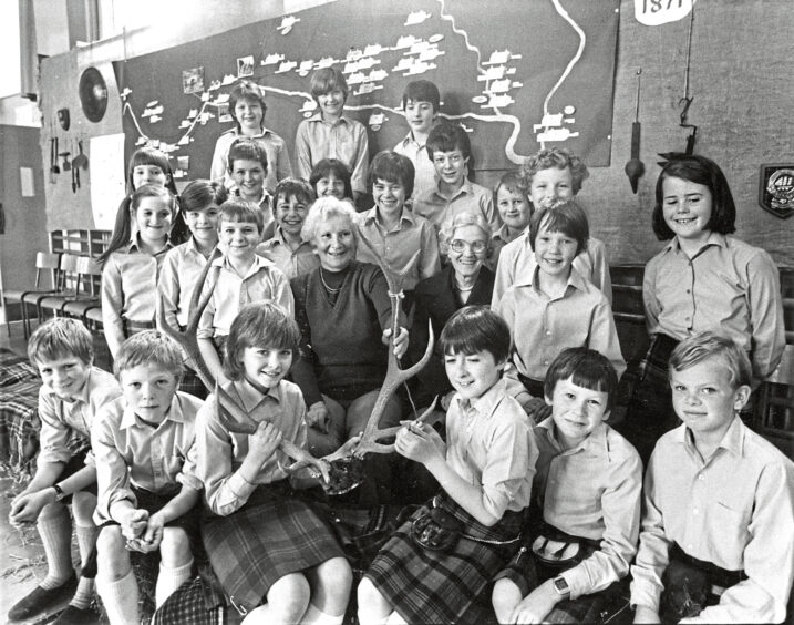 Black and white photo of a group of children in a classroom hold a pair of antlers and smile at the camera