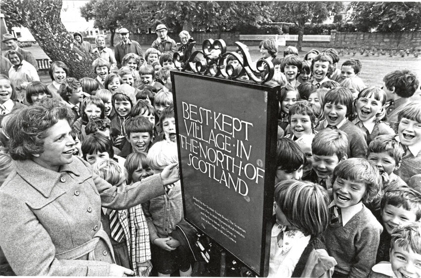 Black and white photo of Mrs Ellen Williamson unveils "Best kept village in the north of Scotland" plaque surrounded by smiling children