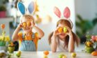Two children wearing Easter themed headgear and holding Easter eggs over their eyes.