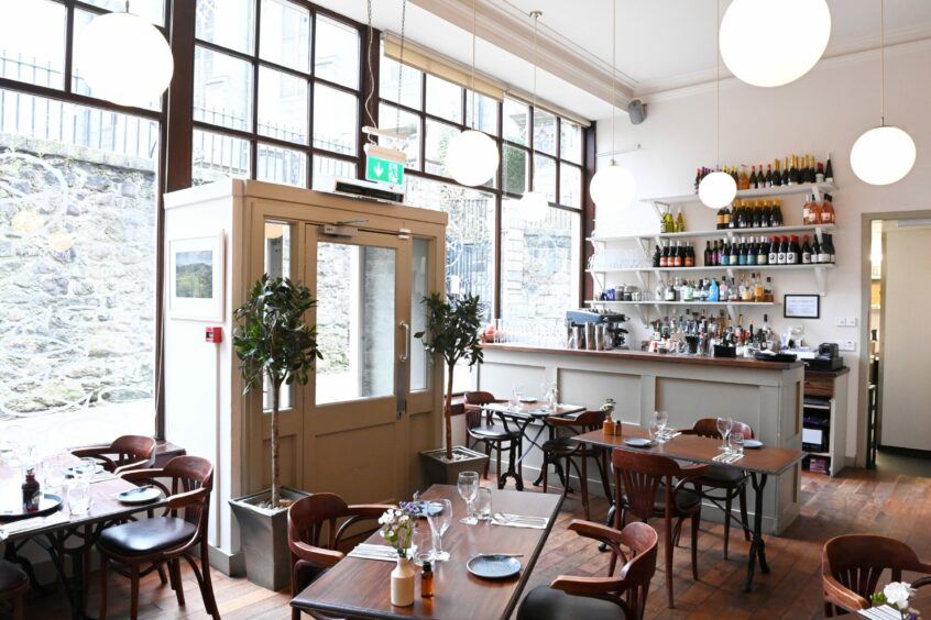 The restaurant from inside, with the large floor to ceiling glass windows and bar, with sleek wooden seating and chairs