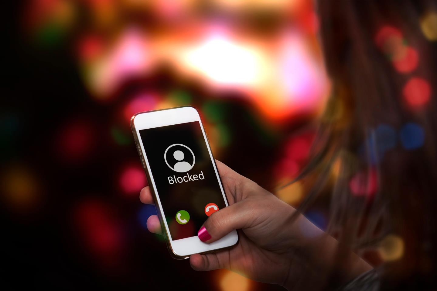 A woman holding a phone with the word 'blocked' on the screen