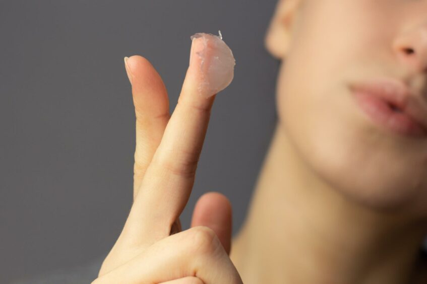 A woman poises ready to apply some Vaseline to her face.