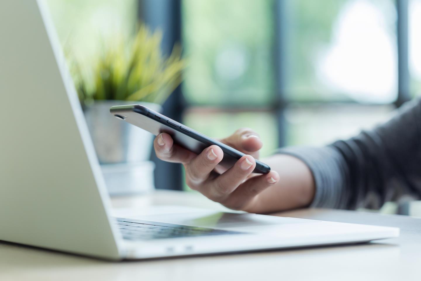 Close up of hand holding phone near a laptop