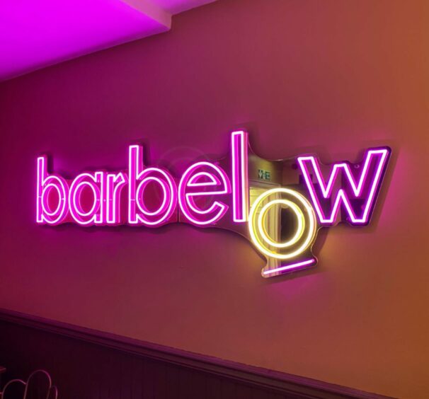 A pink and yellow neon sign reading "barbelow"