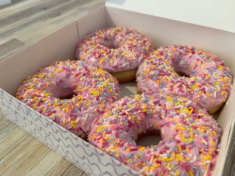 Four pink iced doughnuts with sprinkles