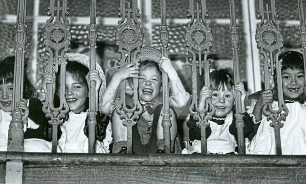 Ashley Road Primary pupils smiling at the camera while peeking through the school railings.