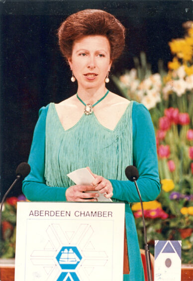 Princess Anne in a light blue dress stands at an Aberdeen Chamber of Commerce podium.