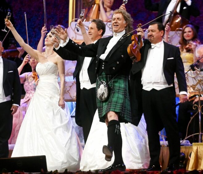 Andre Rieu on stage wearing a kilt with his Johann Strauss Orchestra