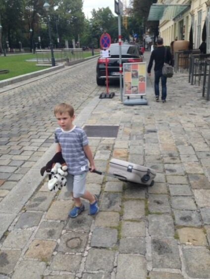 Cameron carrying a suitcase in the street