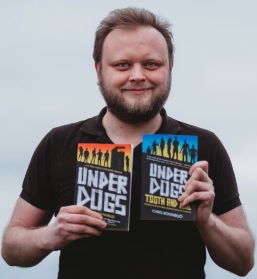 Chris Bonnello holding his two 'Underdogs' novels in each hand