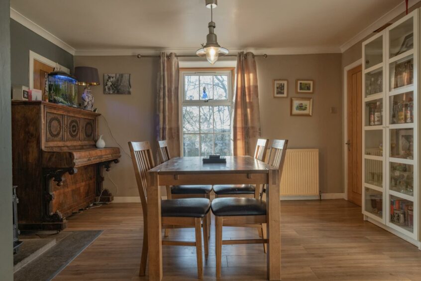 The dining room has wooden floors, table and chairs, and it has a wooden wall piano in the corner.