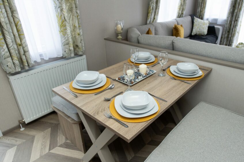 Light wooden table set with yellow placemats and white plates in a neutrally-coloured open-plan space.