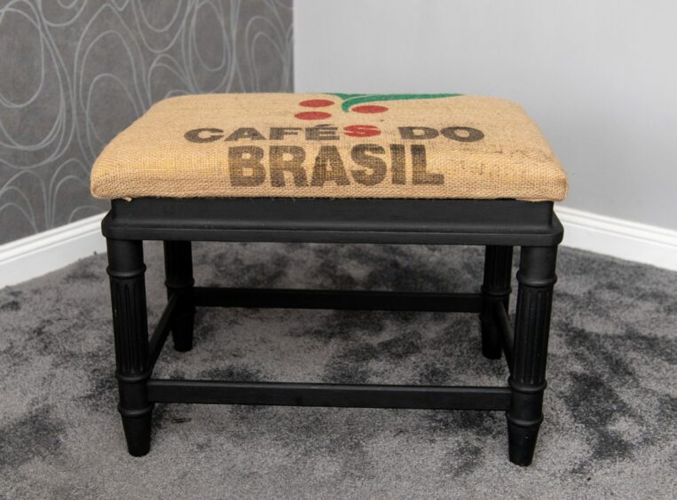 A black stool with the seat covered in jute fabric that reads Cafes do Brasil
