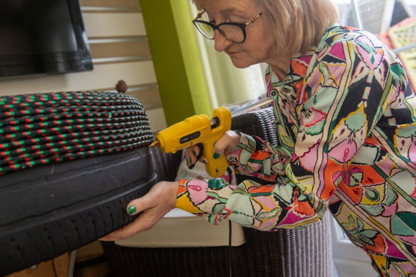 Carol holding a glue gun to an old tyre she is turning into a pouffe