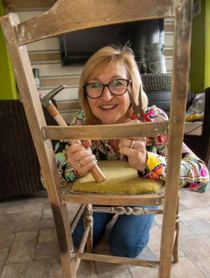 Carol holding her tools and kneeling in front of an old wooden chair