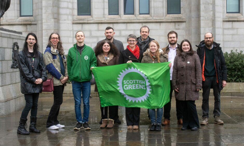 The Scottish Greens candidates standing in Marischal Square and holding a Scottish Greens flag