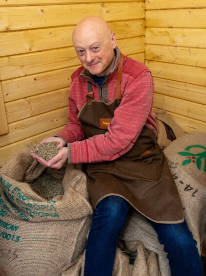 Alan sitting on bags of coffee beans showing a handful of beans that will be roasted to make signature Morningdog Coffee.