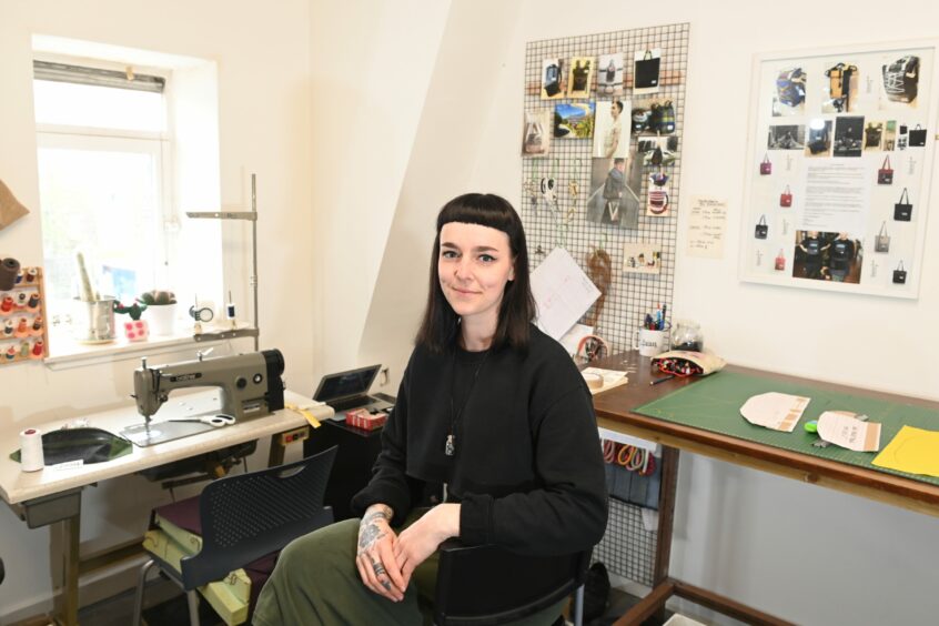 Lucia Gasparidesova in her studio where there is a sewing machine, work table and photographs of clothes and bags.