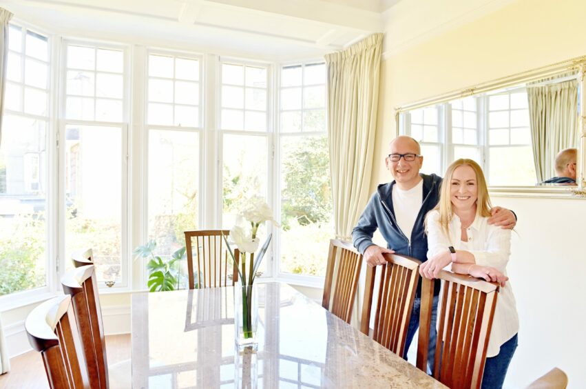 Andrew and Jackie Stannard stand in a bright and light-coloured dining room with large windows.