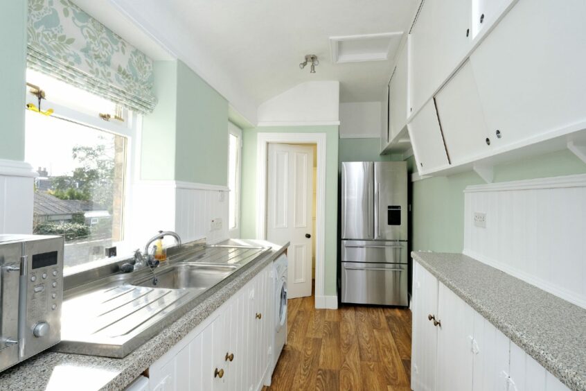 The kitchen has a window over the sink, has white cabinets and is painted light green.