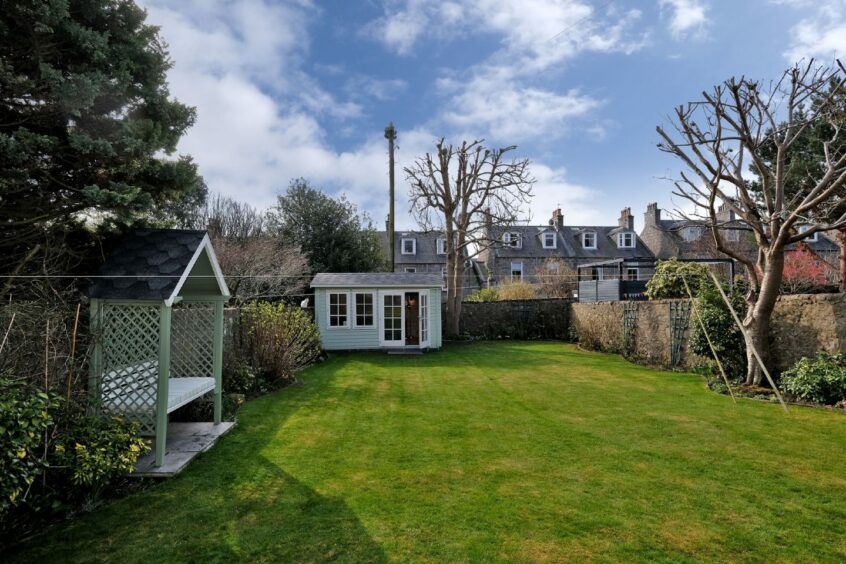 The back garden is hit by sunlight and it has a sitting area and a garden room.