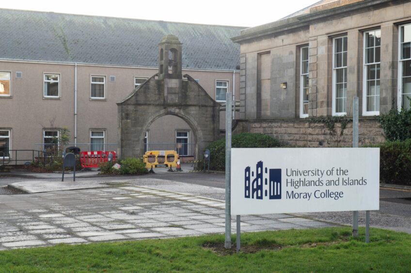 A white sign on metal poles with "University of the Highlands and Islands Moray College" written on it in dark writing, with the building behind.