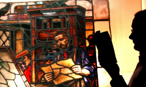 Assistant Keeper Research Chris Croly pictured reading an Aberdeen printers 1620 - 1736 book in front of a stained glass window depicting Edward Raban who was appointed the city's first printer.