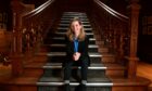 Rebecca Holt sitting on the steps of a wooden grand staircase.