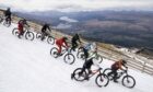 Cyclists descending the slopes in snow for MacAvalanche with green scenery behind.