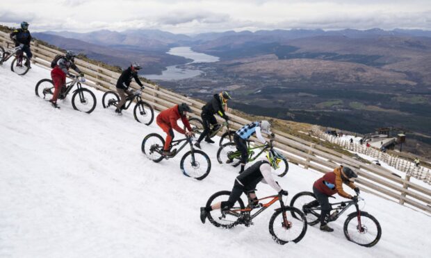 Cyclists descending the slopes in snow for MacAvalanche with green scenery behind.