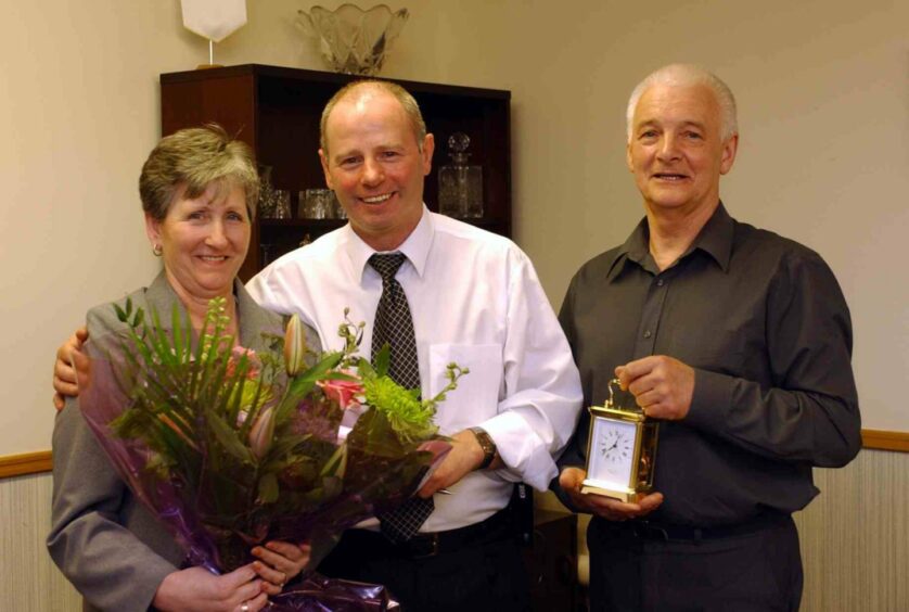 Stewart Milne (centre), with Billy Booth and his wife Barbara, handing over flowers and a clock.