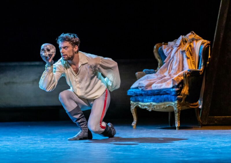 A man on stage during The Scandal At Mayerling, crouching with a skull in his hand