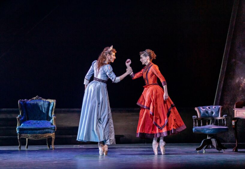 Scottish Ballet's performers on pointe in long dresses, with one grabbing the others arm. 