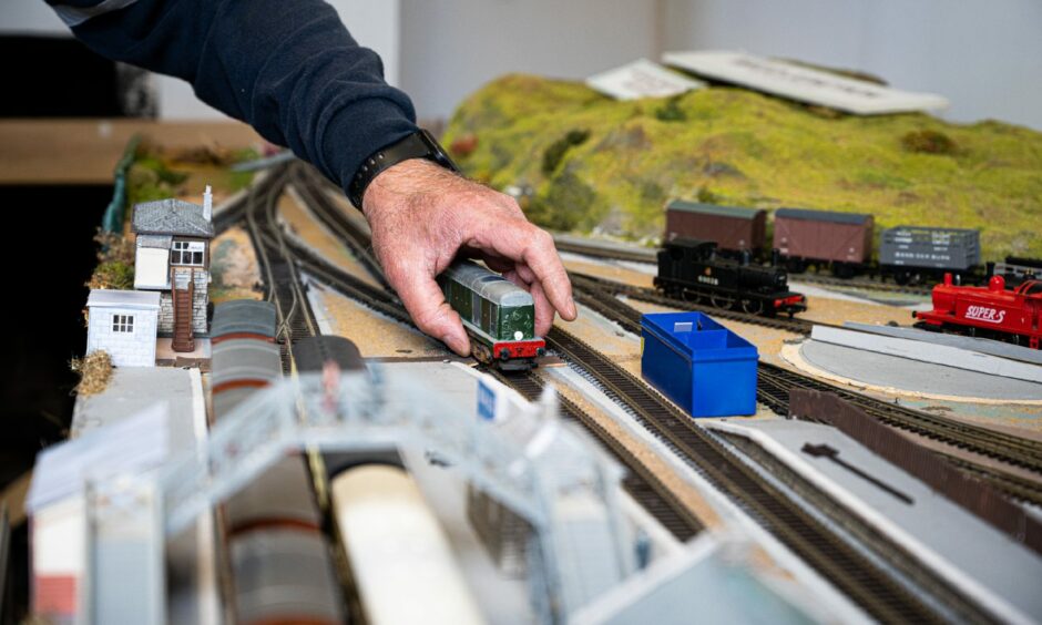 A hand on a miniature train carriage on model train tracks.